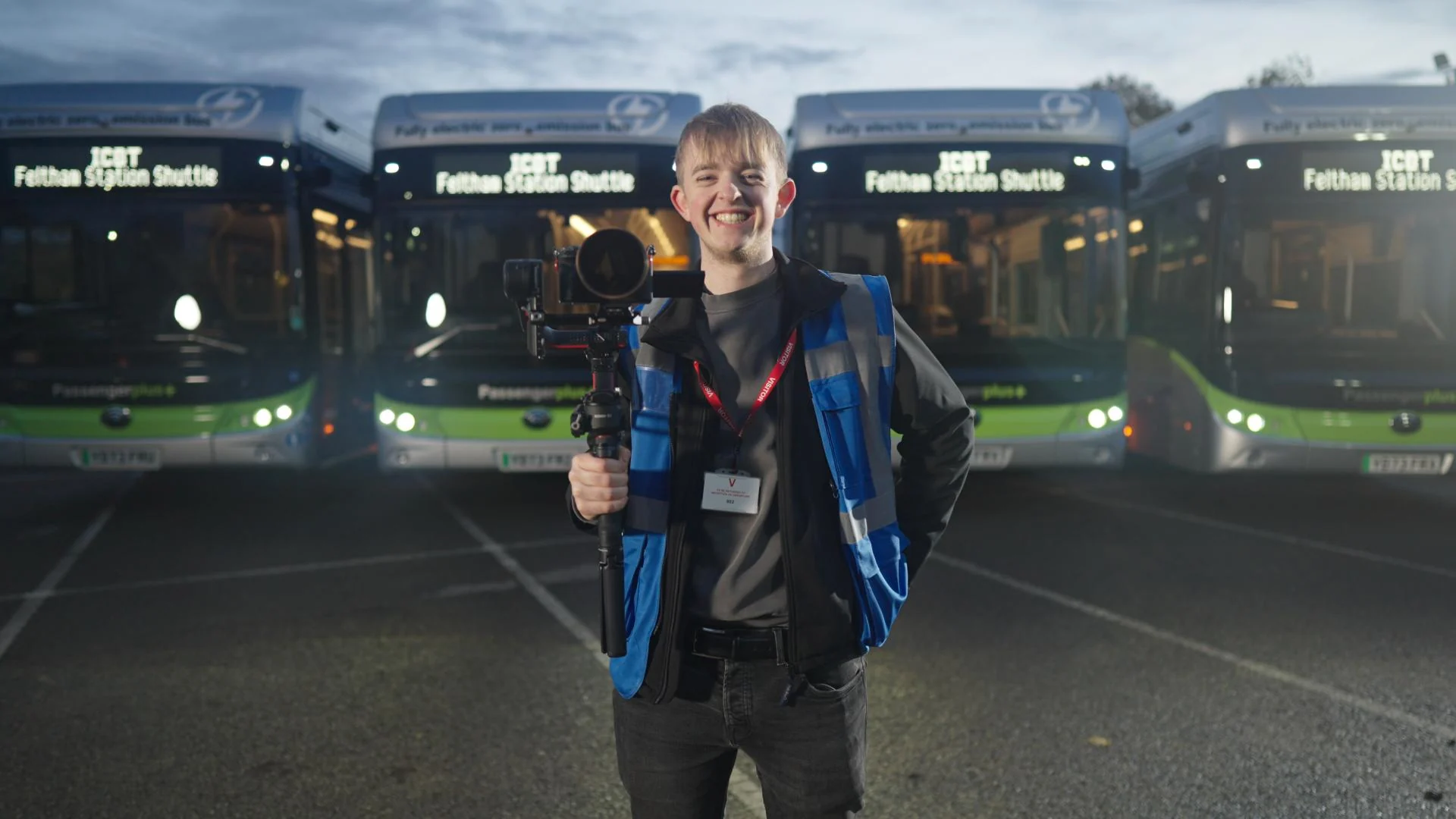 A camera operator with a gimbal rig in front of a line of Passenger Plus electric buses