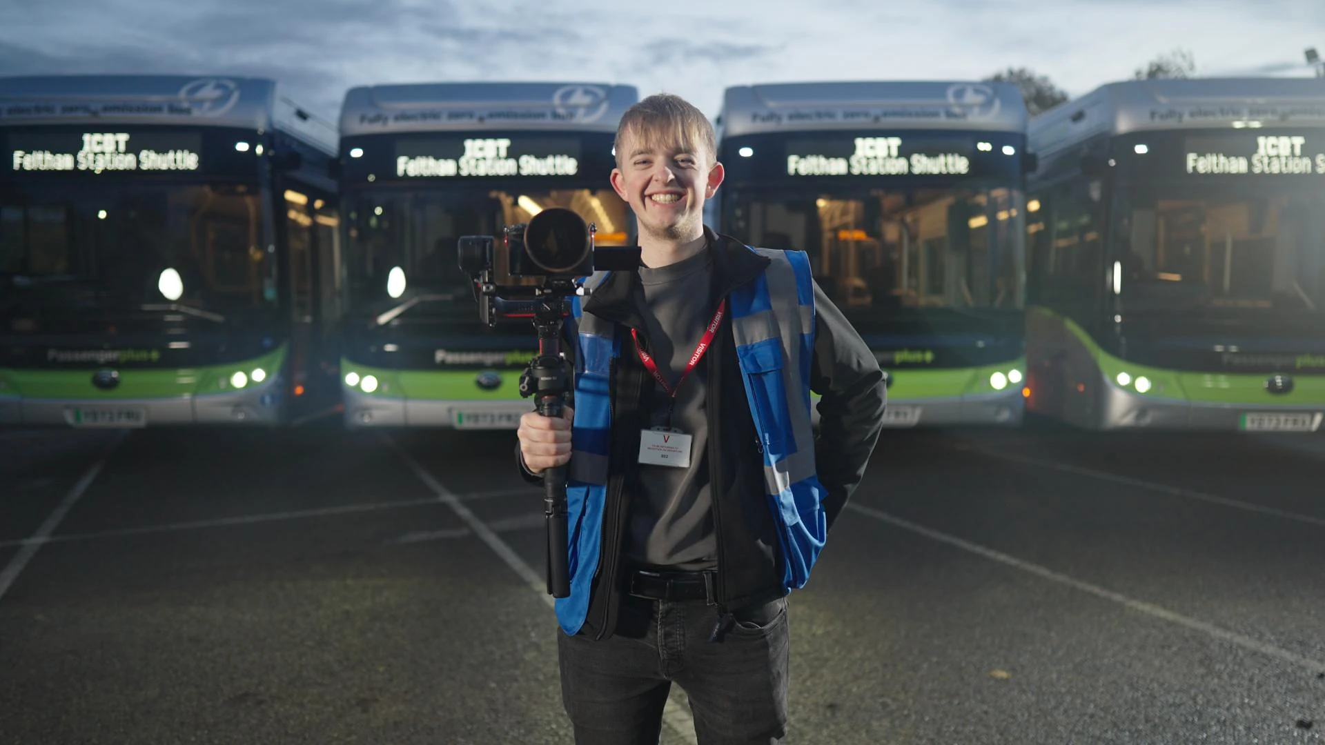 A camera operator with a gimbal rig in front of a line of Passenger Plus electric buses